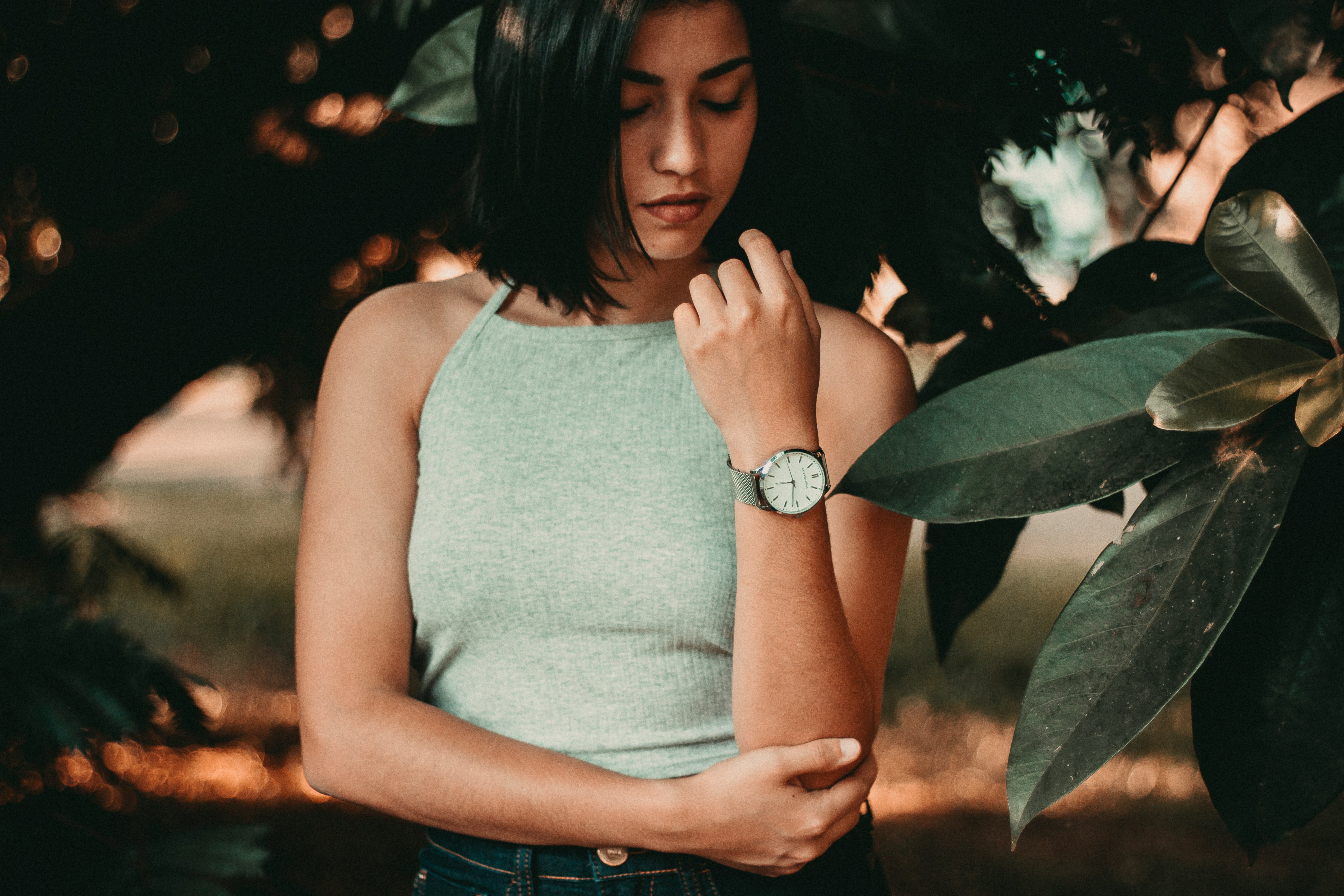 woman standing near green leaf tree while holding her elbow with her right arm